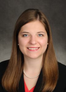 Professional headshot of a smiling woman with long brown hair.
