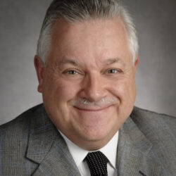 Smiling elderly man in a gray suit and tie.
